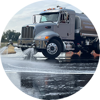 Tanker dispensing water onto pavement at construction site for dust control.