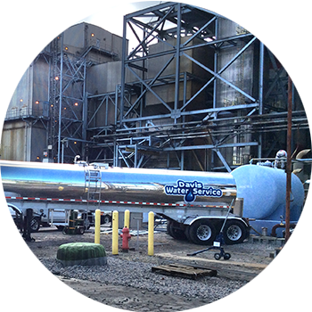 Tanker stationed next to large processing plant, dispensing water.